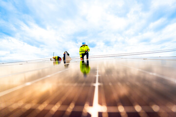 A technician in safety gear inspects solar panels on a metal rooftop, holding a tool. The scene...