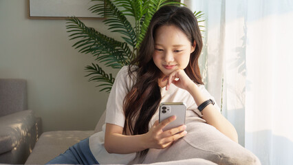 Smiling woman casually using her smartphone while lounging on a couch in a bright living room with...
