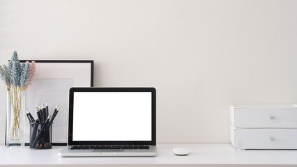 Simple home office with blank photo frame, stationery  and laptop with blank screen for displaying mockups.