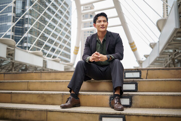 Confident businessman sitting on city steps with modern skyscrapers in the background.