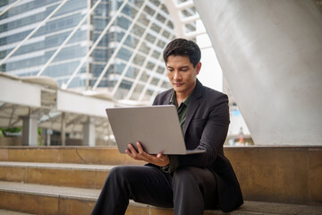 Businessman working remotely with laptop while sitting on outdoor steps in a modern urban environment.