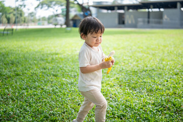 Adorable little boy eating a banana  and exploring the park  on a sunny day.