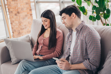 Fototapeta premium Young couple bonding at home while relaxing on the couch with a laptop, enjoying leisure time in a cozy living room setting.