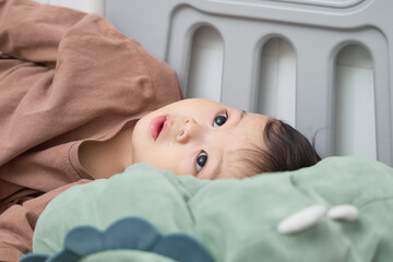 a baby laying on top of a bed next to a white radiator, with a blanket draped over them.