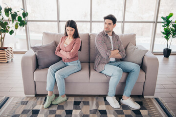 Obraz premium Young couple sitting on a couch expressing emotions in a modern comfortable living room with natural daylight and stylish decor.