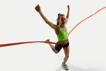 Female runner raises arms in triumph, crossing finish line with energetic expression and vibrant...