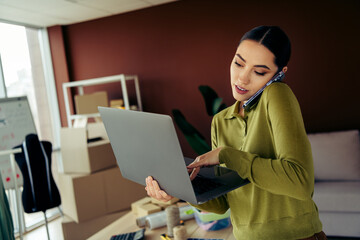 Successful businesswoman multitasking in an office environment handling a laptop and using the...