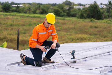 Technician in safety uniform and helmet kneeling on a rooftop, using a drill for precise...