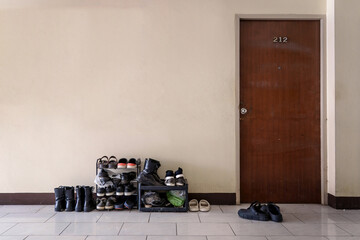 Many pairs of shoes boots, sandals, sneakers on a small old shelf at front door entrance outside room for rent apartment.
