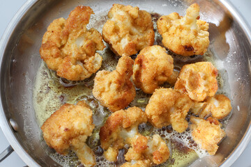 Golden cauliflower inside fry pan with hot oil