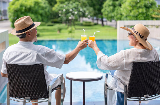 happy senior couple enjoy talking with freshy drink on table,sitting,relaxing by the pool,elderly people travel destination tropical resort and spa on summertime