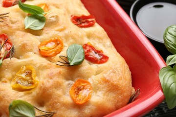 Delicious focaccia with tomatoes and spices in baking dish on table, closeup