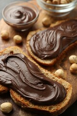 Slices of bread with chocolate spread and hazelnuts on wooden board, closeup