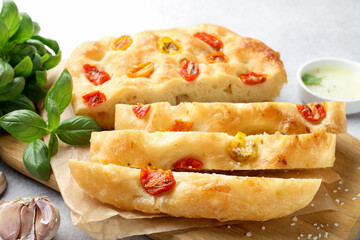 Cut delicious focaccia with tomatoes, spices and oil on gray table, closeup