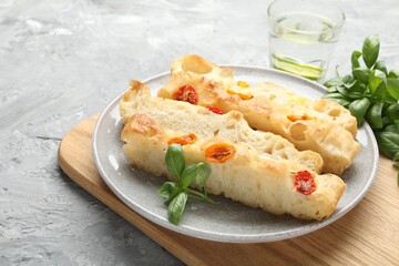 Pieces of delicious focaccia with tomatoes, basil and glass of water on gray textured table, closeup