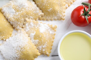 Uncooked ravioli, tomatoes and oil on white wooden table, closeup