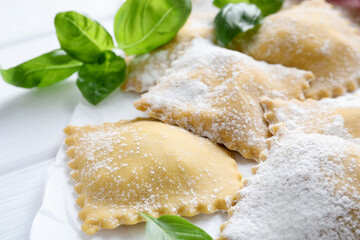 Uncooked ravioli and basil on white table, closeup