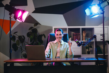 Young female professional hosting live podcast in a stylish home studio office with modern lighting...