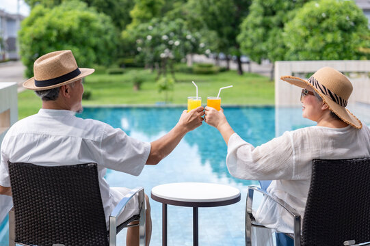 happy senior couple enjoy talking with freshy drink on table,sitting,relaxing by the pool,elderly people travel destination tropical resort and spa on summertime