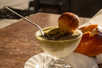 Sicilian pistachio granita with brioche dipped into glass cup at outdoor breakfast table