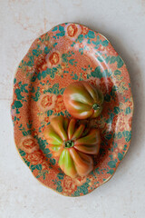 Two ripe tomatoes on a detailed floral plate, perfect for e-commerce food listings. Highlight fresh produce in your online store. Suited for grocery, organic products, or farmer’s market promotions.