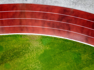 Aerial view of a red running track with marked lanes and curved lines. Athletic stadium section...