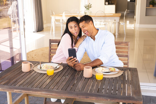 Couple taking selfie at breakfast table, playfully sticking out tongues