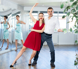 Guy and girl in stage costumes, under guidance of mentor, practice tango in choreographic studio....
