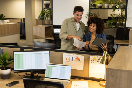 Collaborating diverse coworkers reviewing document behind office cubicle desk, with tablet