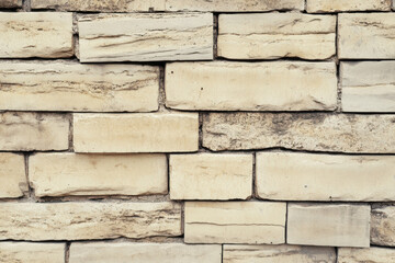 Tan bricks are stacked together to form a wall in the building, creating a rough texture with varied surface details and neutral color for background.