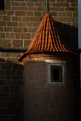 A close-up view highlights a round, turret-like architectural feature on a historical building. The turret has a conical roof covered in textured reddish-orange tiles and features a small window © Bohdan Hroshev