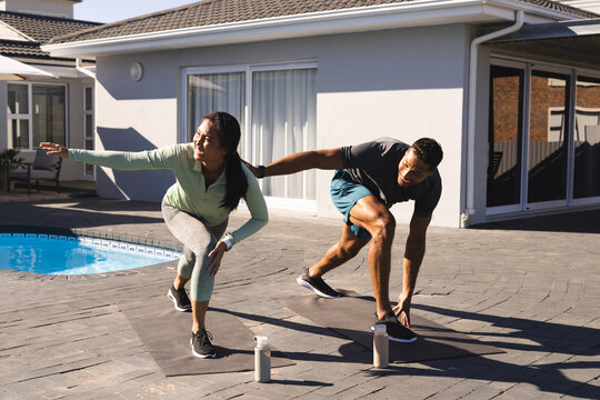 Couple exercising outdoors, stretching and balancing on yoga mats by pool