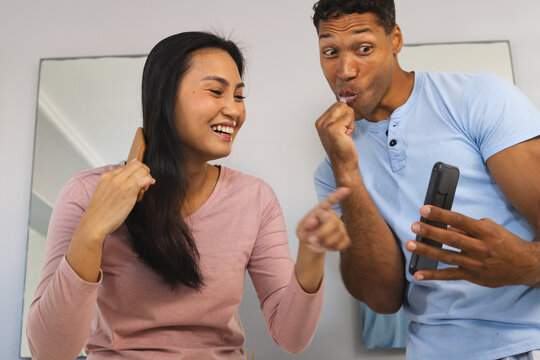 Couple laughing together while brushing teeth and looking at smartphone at home