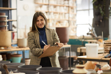 Smiling ceramics studio owner doing inventory in a pottery workshop