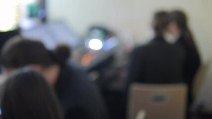 Blurry image of people sitting at desks with some of them using cell phones. Scene is casual and relaxed, as people are working and using their phones