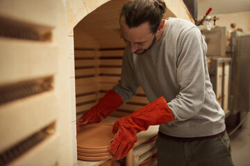 Ceramist taking plates from a workshop kiln after firing