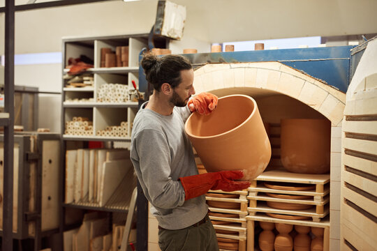 Ceramist removing a large clay pot from a workshop kiln