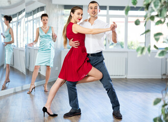 Man and girl take dance lessons from experienced teacher. Couple in stage costumes practices tango...