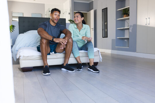 Couple relaxing on bed after workout, smiling and enjoying conversation at home