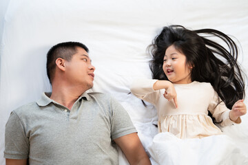 Asian father and daughter talking on bed. Family enjoy playing and spending time together at home