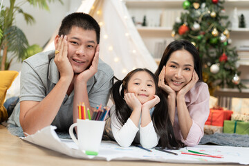 Happy Asian family with chin on hand pose, lying on floor with cozy tent background in the living room at home. Daughter and parent playing and spending time together