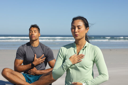 Couple meditating on beach, practicing mindfulness and relaxation by ocean