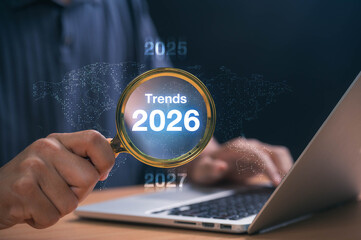 Businessman analyzing trends 2026 with magnifying glass over laptop, representing future technology, global forecasting, strategic growth planning and digital innovation for business development