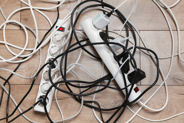 Extension power boards overloaded with plugs on wooden floor, top view