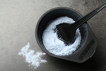 Bowl with hair bleaching powder and brush on grey table, top view