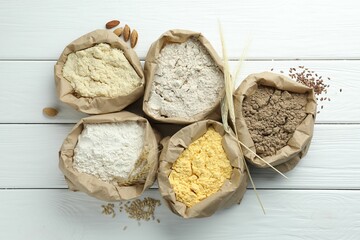 Different types of flour in paper bags on white wooden table, flat lay