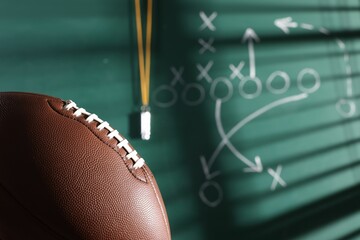 American football ball near chalkboard with scheme of game, closeup