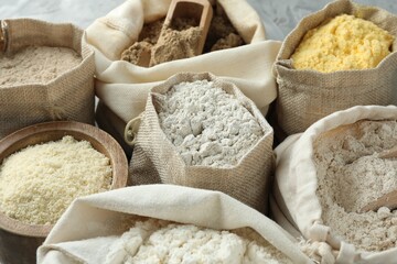 Different types of flour in bags on grey table, closeup