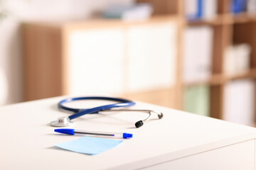 Doctor's workplace. Stethoscope, pen and sticky note on white table in medical office, closeup. Space for text