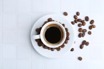 Aromatic coffee in cup and beans on white tiled table, flat lay